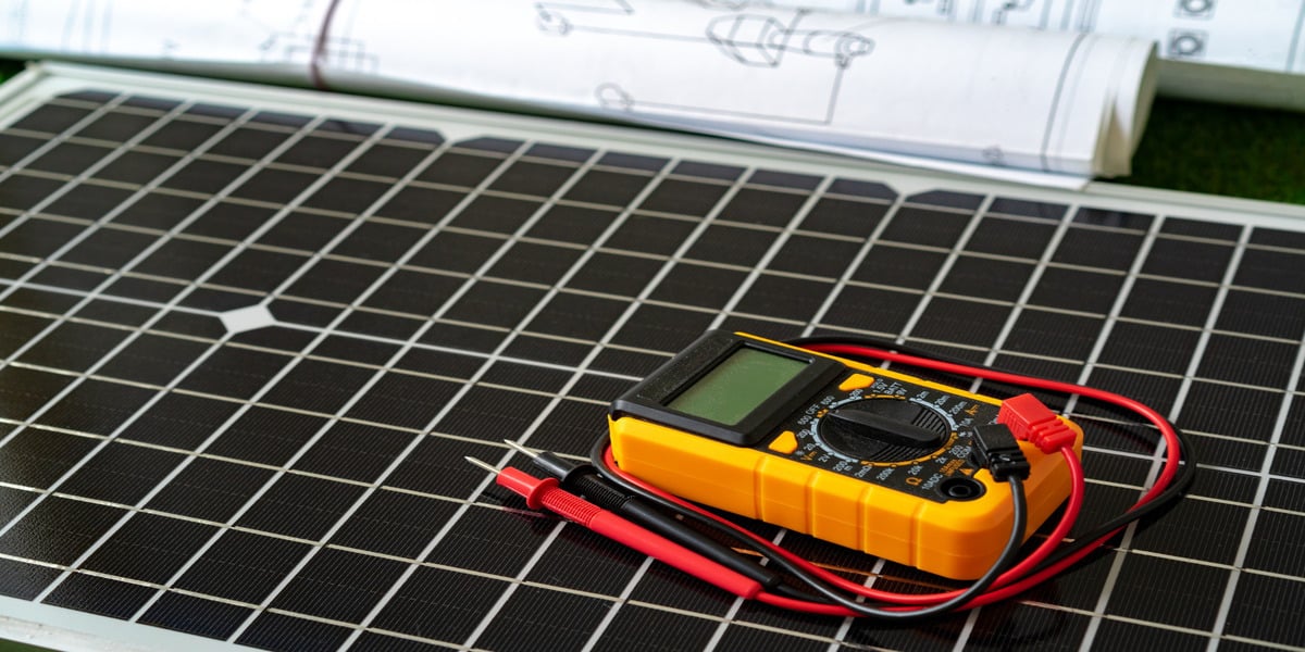 DIY Solar Power Systems: Are They Worth It? Expert Electric tests a DIY solar power system panel voltage with a yellow multimeter.