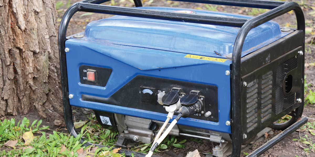A small blue portable generator beside a tree, wired for temporary use. Home Backup Generators like this from Expert Electric are budget-friendly solutions for powering essentials during brief outages in cabins, campsites, or urban homes with limited backup needs.