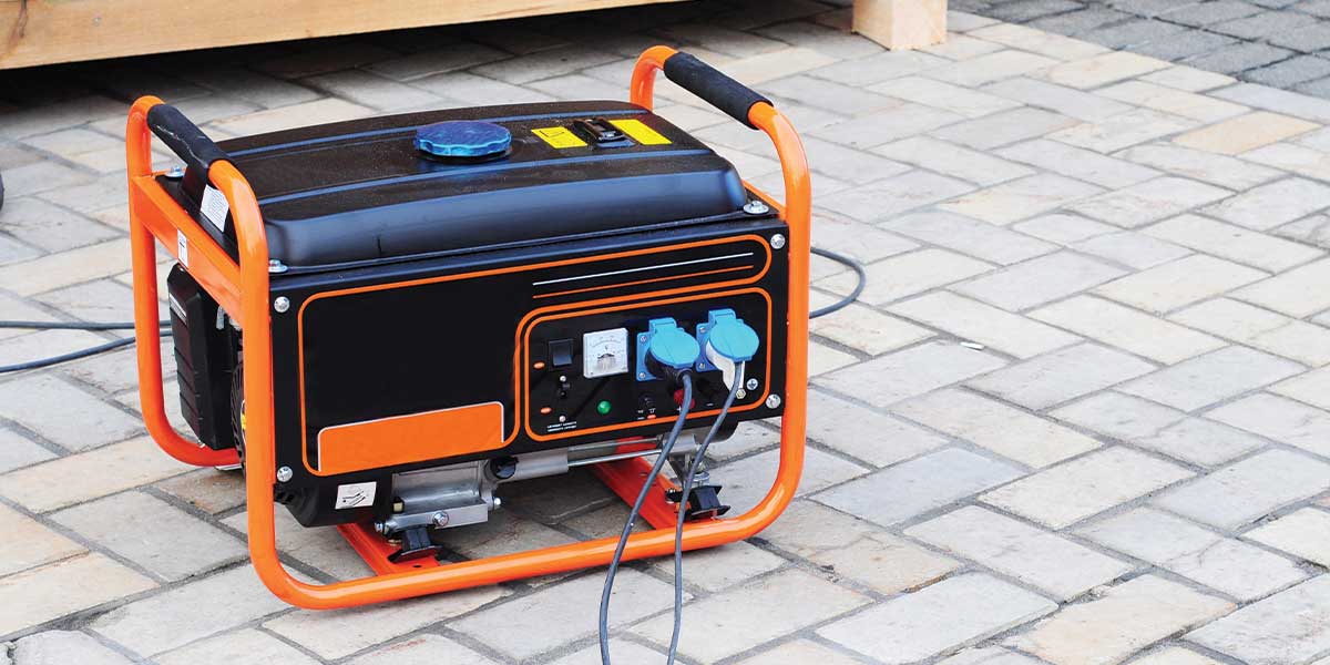 A compact, portable generator with dual outlets and orange framing sits on a brick patio, ready for manual use. This unit represents the portable type of Home Backup Generators available through Expert Electric—perfect for short-term emergency power or mobile use.