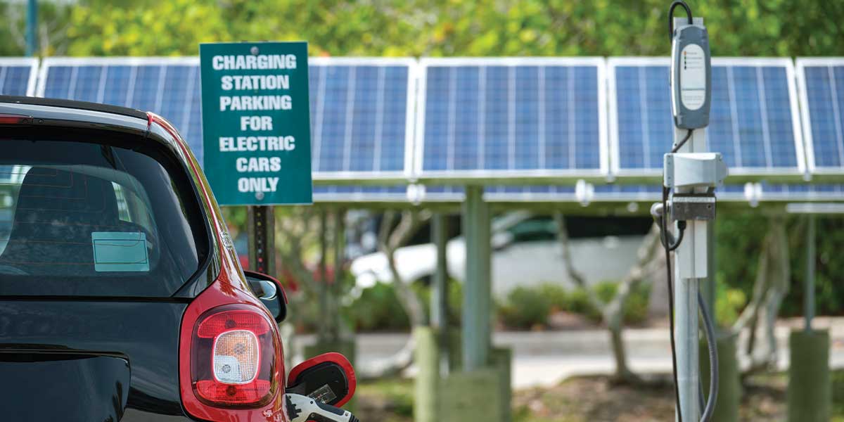 Explore solar energy for beginners with Expert Electric. This image shows an electric car charging at a solar-powered station, backed by solar panels, demonstrating how renewable energy seamlessly integrates into daily life for eco-friendly and cost-effective solutions.