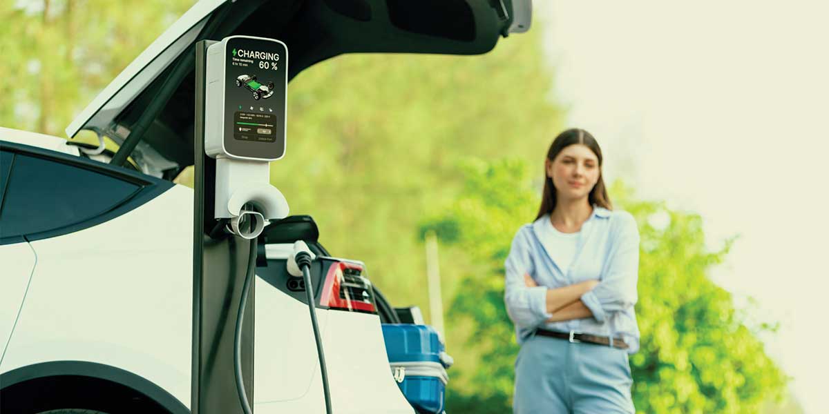 A woman standing by an electric car charging station, emphasizing infrastructure development in the Evolution of Electric Vehicles.