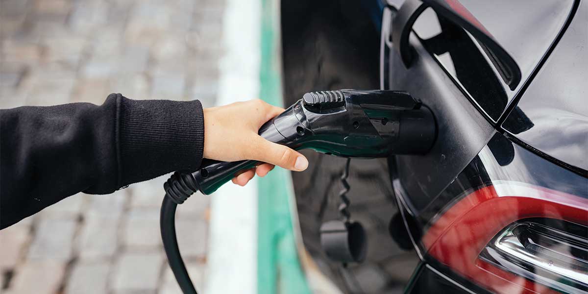 A person plugging a charging cable into an electric car, symbolizing the growth in EV adoption as part of the Evolution of Electric Vehicles.