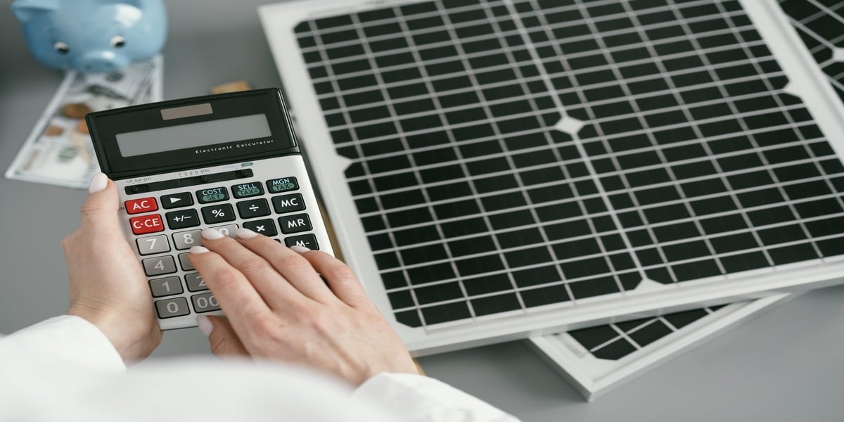 Close-up of a hand using a calculator next to solar panels and money, symbolizing cost savings and return on investment. This illustrates how Expert Electric guides homeowners in calculating benefits from 2025 solar incentives and rebates programs.