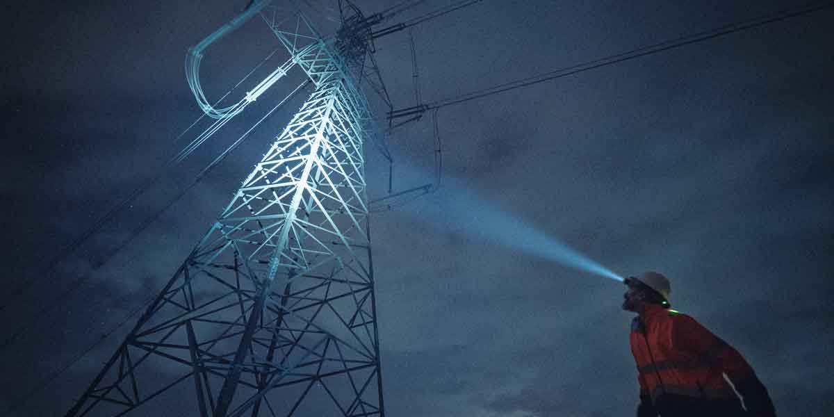 Electrician looking up with headlamp at Electrical Tower in a blackout.