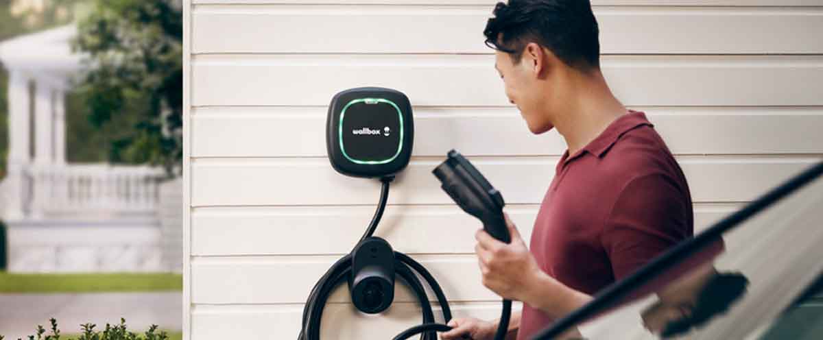 Man taking Wallbox EV Charger connector off the wall towards his car.